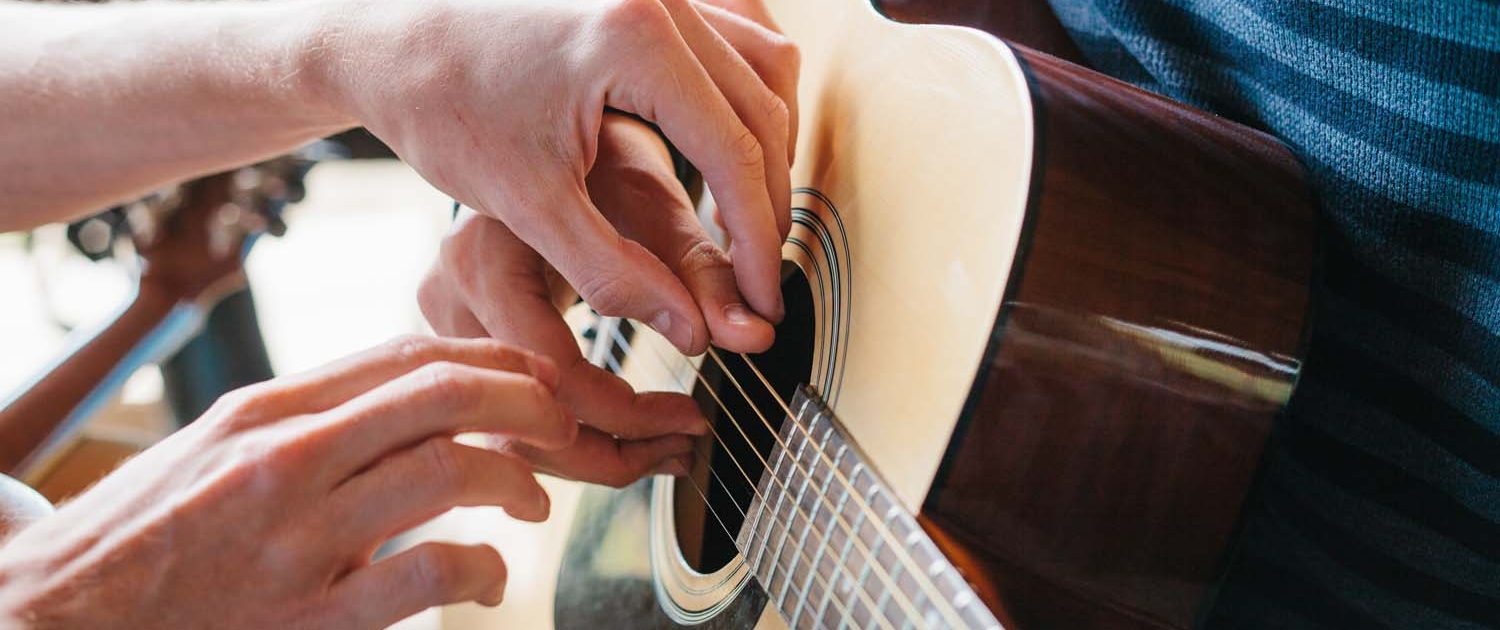 teacher helping guitar pupil to place fingers on the guitar