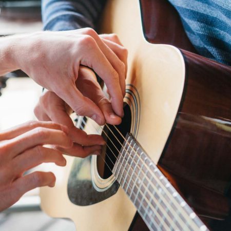 teacher helping guitar pupil to place fingers on the guitar