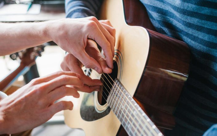 teacher helping guitar pupil to place fingers on the guitar